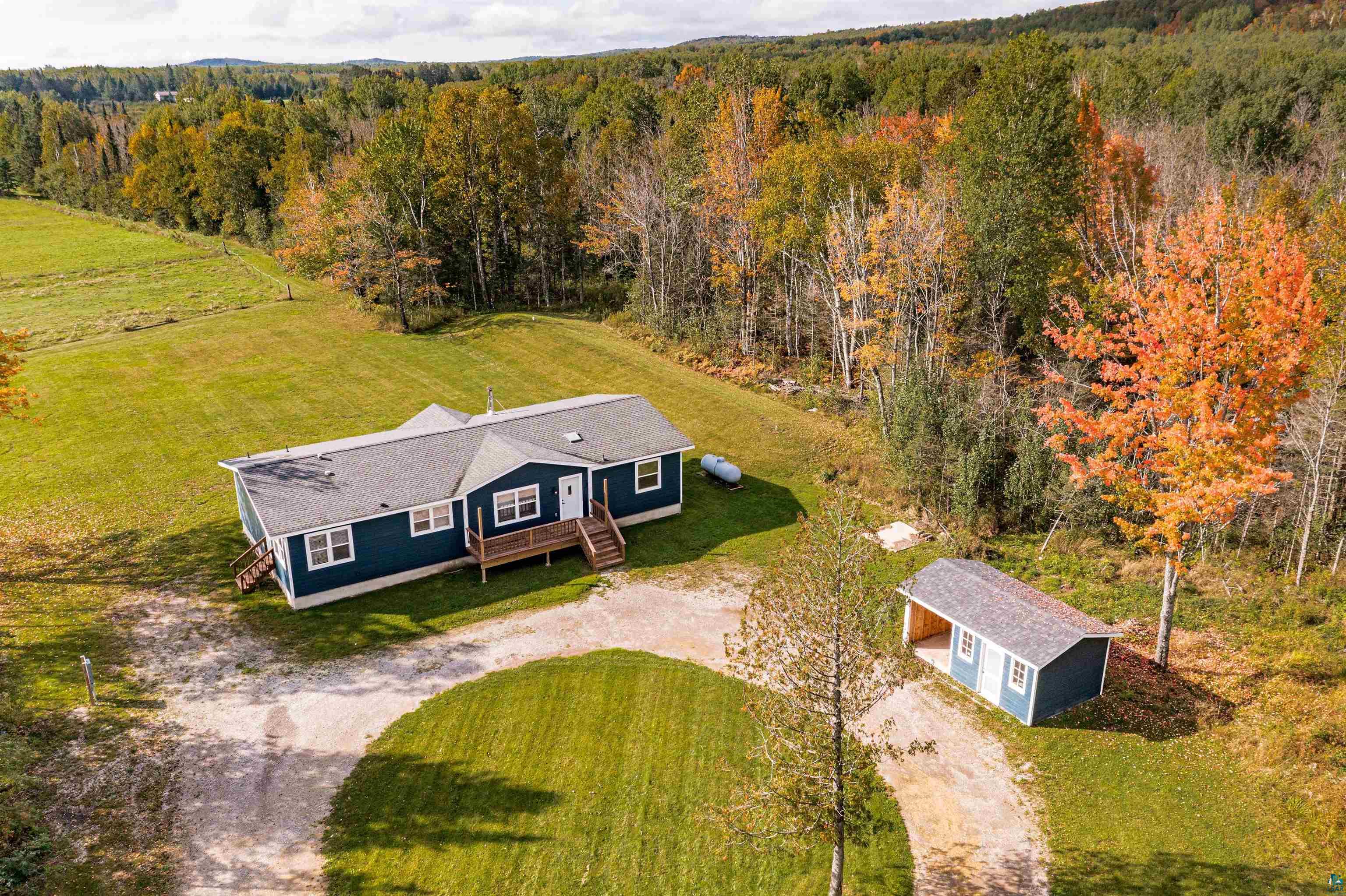 Expansive property featuring a blue-sided residence with white trim, a gravel driveway, and surrounding green lawn