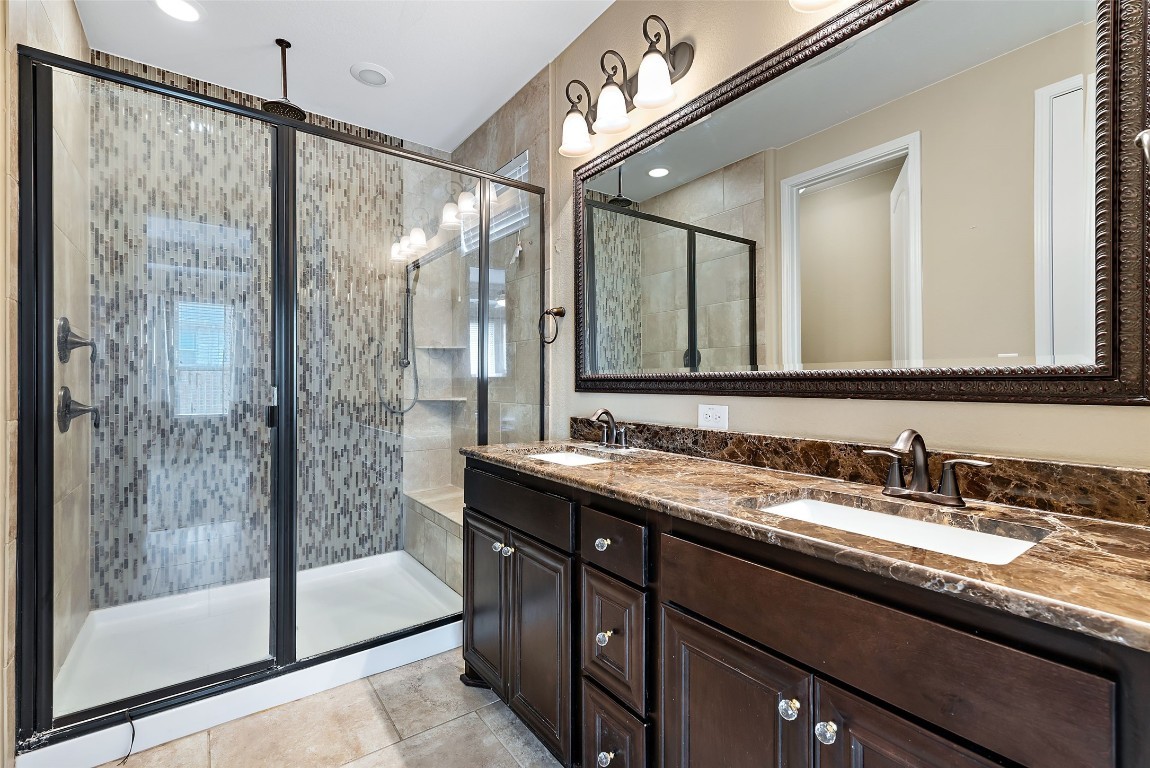 2000 Manada Trail Leander, TX 78641 - Photo 22 of 36 Dual vanity with rich cabinetry and a spacious walk-in shower with tile surround.