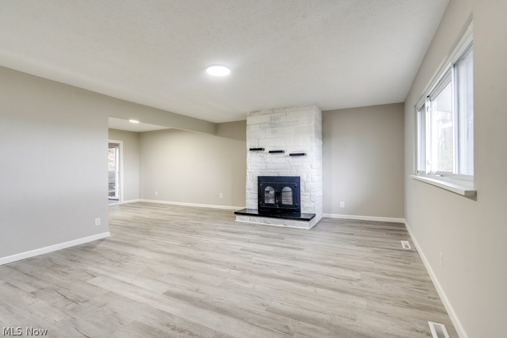 4596 Hattrick Road Rootstown, OH 44272 - Photo 8 of 45 Unfurnished living room featuring a healthy amount of sunlight, a fireplace, light hardwood / wood-style floors, and a textured ceiling