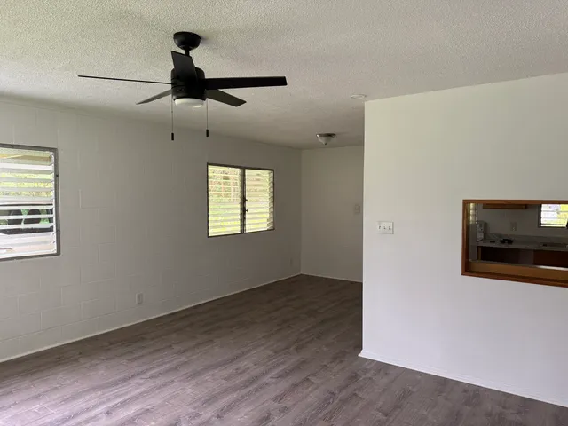 a view of a livingroom with wooden floor a ceiling fan and windows