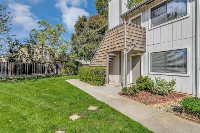a view of a white house next to a yard with plants and trees
