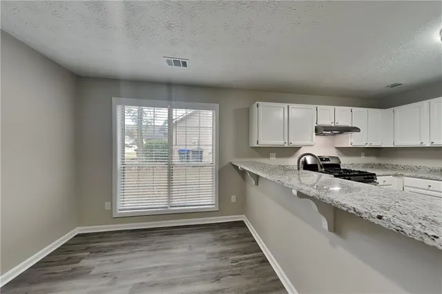 a large kitchen with granite countertop a stove a sink and dishwasher wooden cabinets with wooden floor