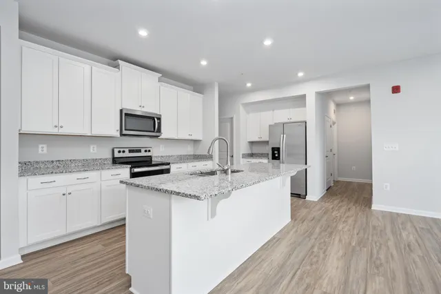 a kitchen with kitchen island granite countertop a stove top oven a sink and white cabinets