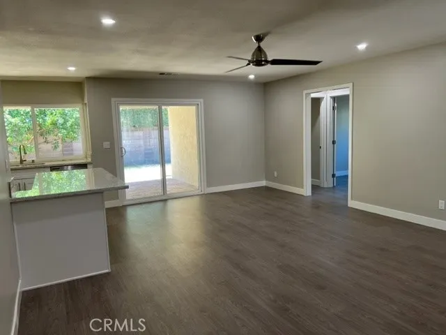 an empty room with wooden floor a ceiling fan and kitchen view