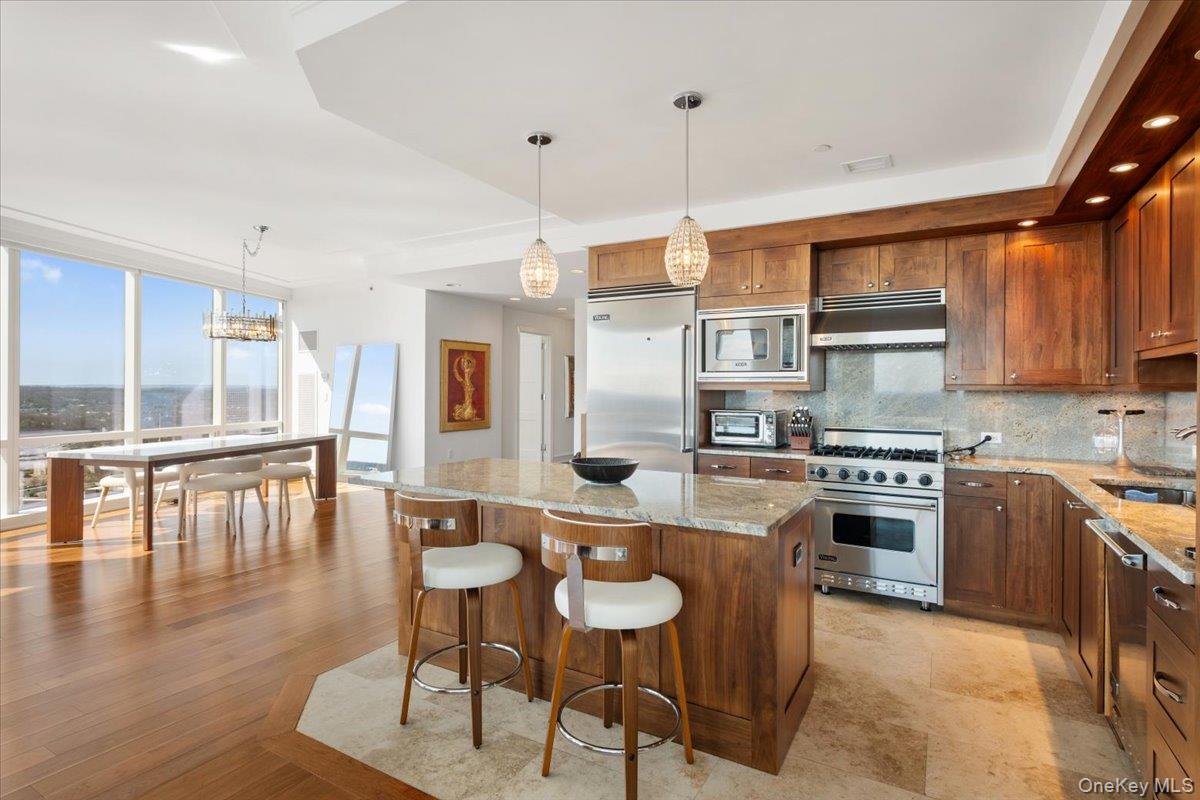 5 Renaissance Square, Unit PH 3E White Plains, NY 10601 - Photo 12 of 26 a kitchen with stainless steel appliances granite countertop a stove top oven a sink a dining table and chairs with wooden floor