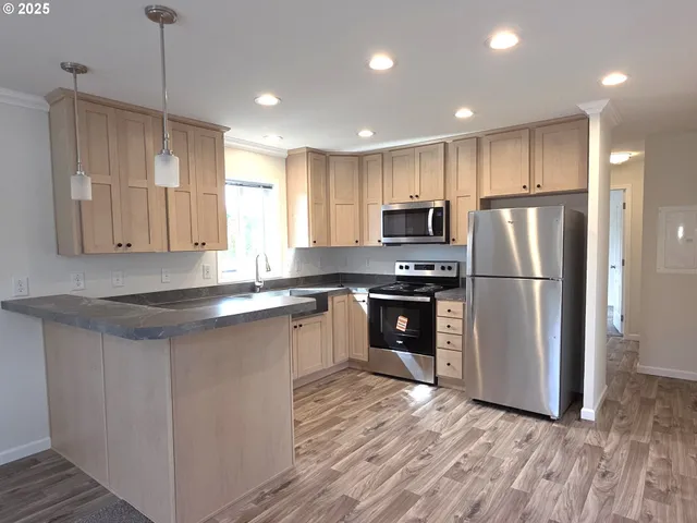 a kitchen with stainless steel appliances granite countertop a refrigerator a sink dishwasher a stove and white countertops with wooden floor