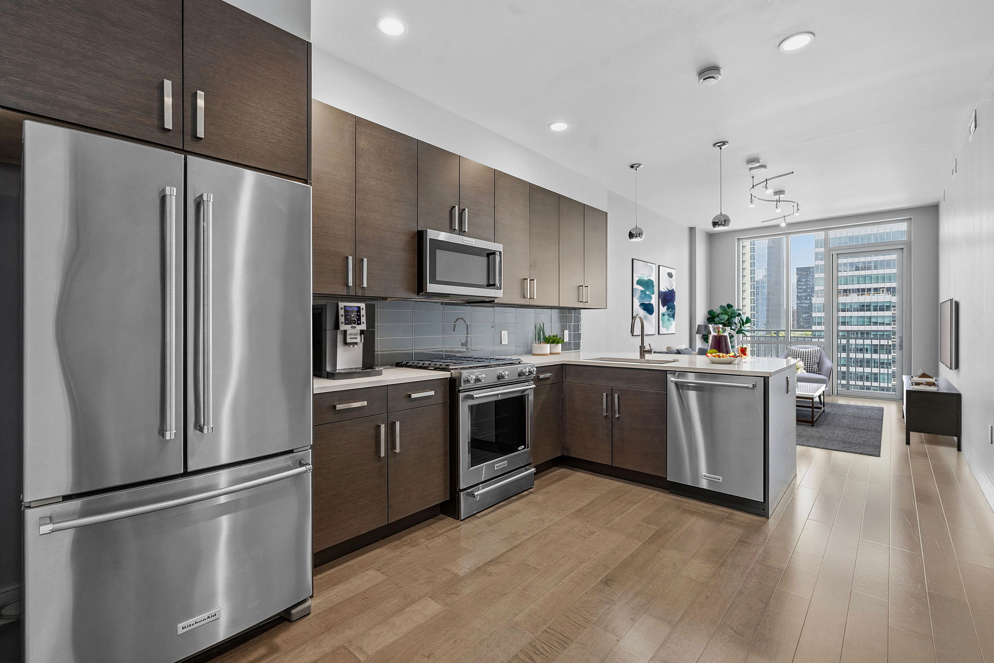 222 West Avenue, Unit 2207 Austin, TX 78701 - Photo 1 of 30 Modern kitchen featuring stainless steel appliances, dark wood-finish cabinetry, light countertops, a gray tile backsplash, and light wood-finish flooring