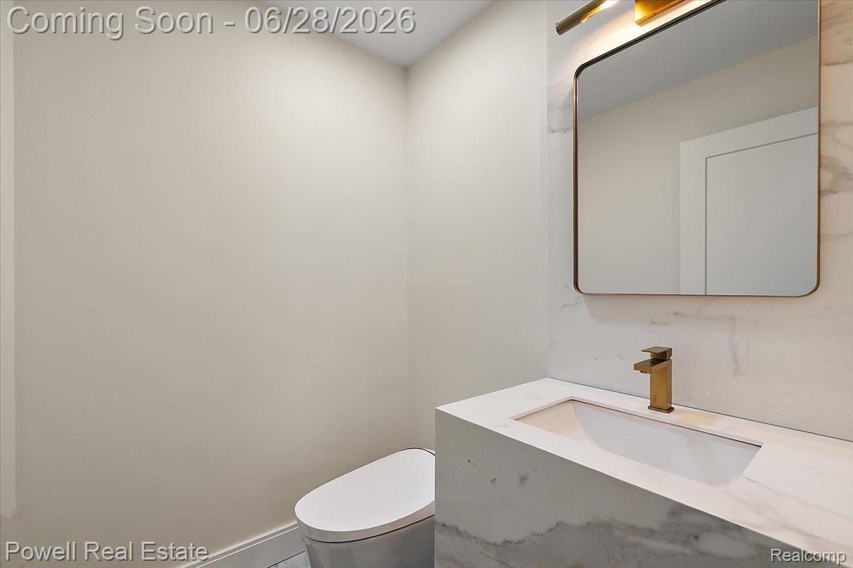 1447 Ravineview Court, Unit C12 Bloomfield Hills, MI 48304 - Photo 11 of 49 Vanity area featuring a waterfall countertop with integrated sink, brass-finish faucet, framed mirror, and modern wall sconce