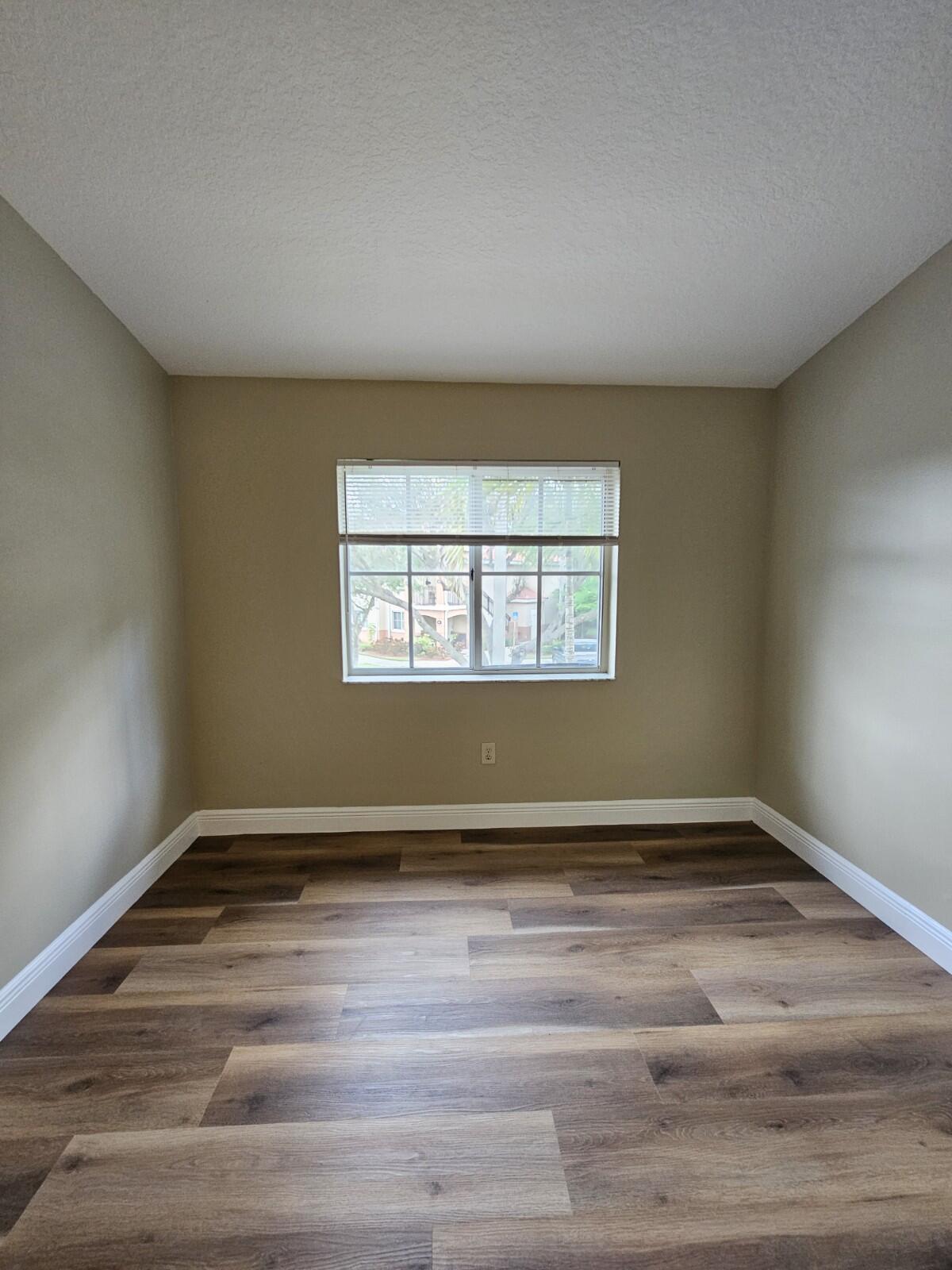 3490 Briar Bay Boulevard, Unit 206 West Palm Beach, FL 33411 - Photo 8 of 25 a view of an empty room with wooden floor and a window