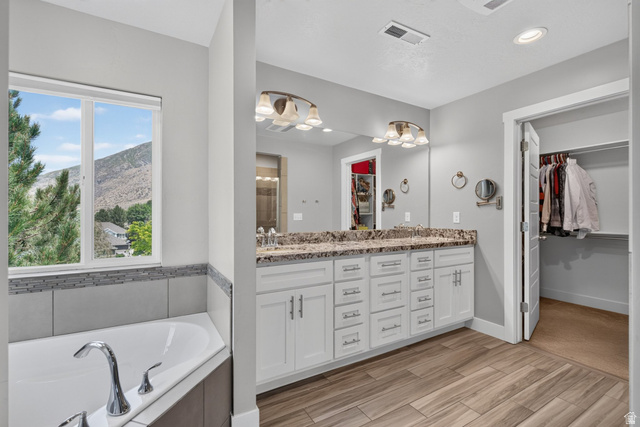 1263 East 1200th South Springville, UT 84663 - Photo 18 of 60 Bathroom featuring a corner soaking tub with a tiled surround, a double vanity with a stone countertop and dual sinks, wood-finish flooring, and a walk-in closet