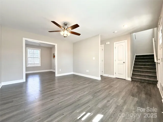 a view of an empty room with wooden floor and a ceiling fan
