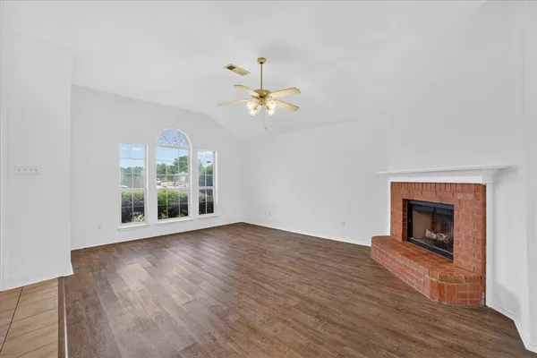 a view of an empty room with wooden floor fireplace and a window