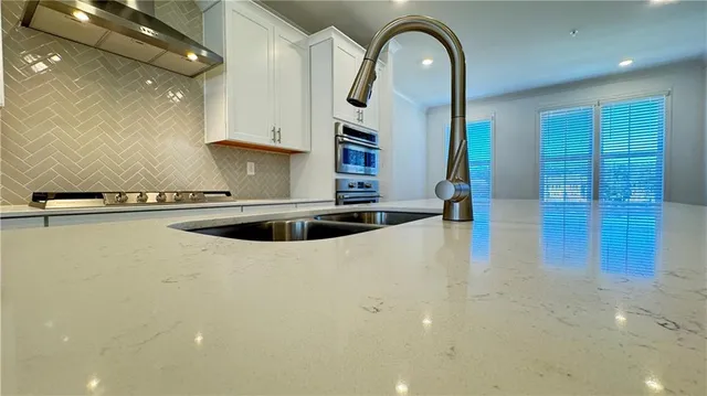 a large kitchen with stainless steel appliances kitchen island a stove a sink a refrigerator and white cabinets with wooden floor