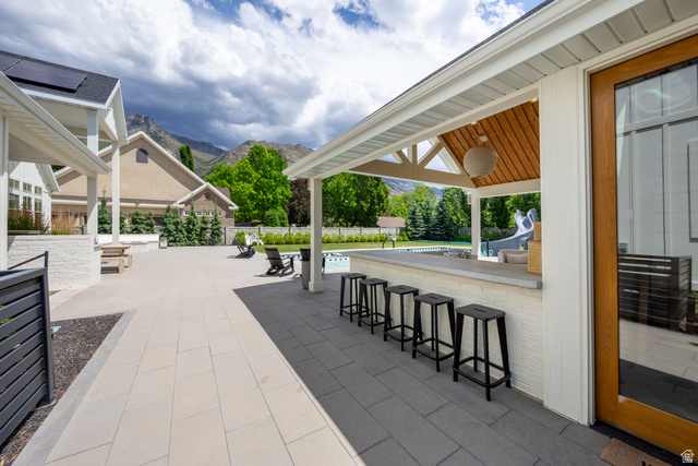 630 East Center Street Alpine, UT 84004 - Photo 83 of 115 Expansive outdoor patio with large format pavers, a covered bar area featuring a wood-finish ceiling, an outdoor pool, mature landscaping, and mountain scenery