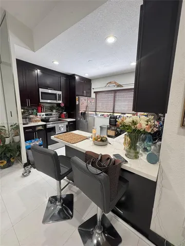 a room with stainless steel appliances kitchen island granite countertop a table chairs and a refrigerator