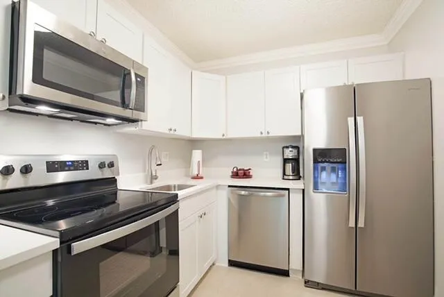 a kitchen with stainless steel appliances a refrigerator a stove top oven a sink dishwasher and white cabinets