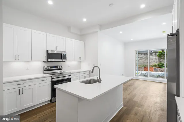 a large kitchen with stainless steel appliances kitchen island granite countertop a stove a sink a refrigerator and a white cabinets with wooden floor