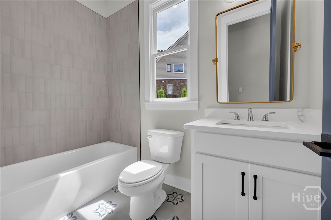 2476 St Martin Way Monroe, GA 30656 - Photo 28 of 75 Guest Bathroom featuring a white bathtub, gray vertical subway tile surround, white vanity with integrated sink, gold-framed mirror, and patterned floor tiles