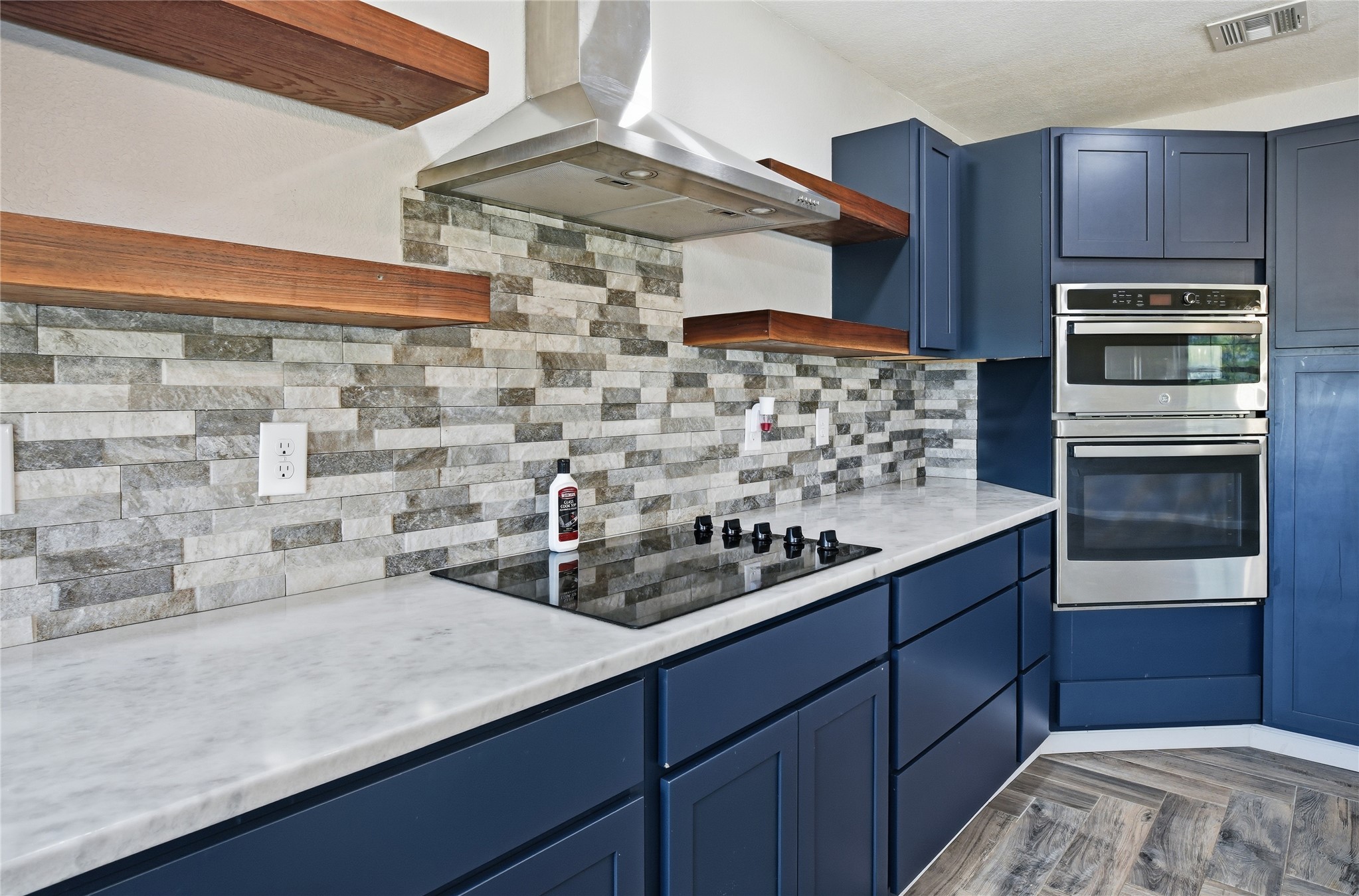 81232 South 4775 Road Stilwell, OK 74960 - Photo 26 of 50 Modern kitchen featuring blue cabinetry, a stainless steel range hood, a tiled backsplash, wood-finish shelving, and a built-in oven and microwave combination