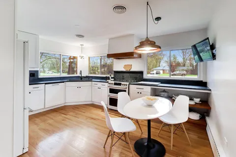 a kitchen with stainless steel appliances granite countertop a stove a sink dishwasher a dining table and chairs with wooden floor
