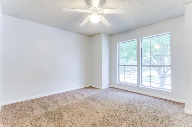 an empty room with chandelier fan and windows