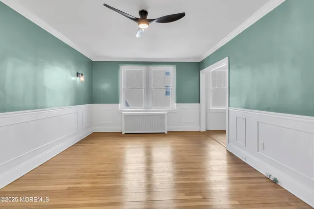 a view of an empty room with wooden floor and a ceiling fan