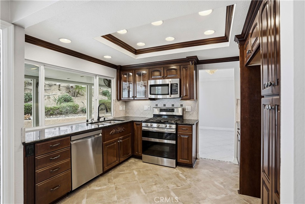 6568 Balzac Circle Riverside, CA 92506 - Photo 22 of 62 Kitchen is brethtaking! Double ovens, microwave above. Dual stainless steel sink with dishwasher. Cuboards to the left of microwave have gorgoeous glass overlays to display fine china, etc. Tons of pantry cupboards on the right. Alumawood patio the length of the house outside for entertaining. Notice the architectual details in the ceiling. Dark wood cupboards trimed with exceptional detail. Granite on the countertops.