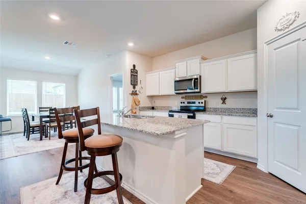 a kitchen with stainless steel appliances granite countertop a stove a sink a microwave a dining table and chairs with wooden floor