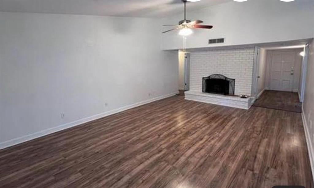 4422 Galaxie Road Garland, TX 75044 - Photo 4 of 11 Spacious living area featuring wood-finish flooring, a white brick fireplace with a decorative metal screen, and a ceiling fan with integrated lighting