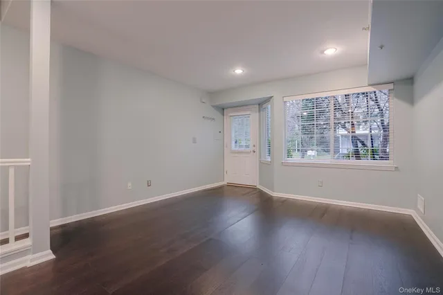 a view of an empty room with wooden floor and a kitchen