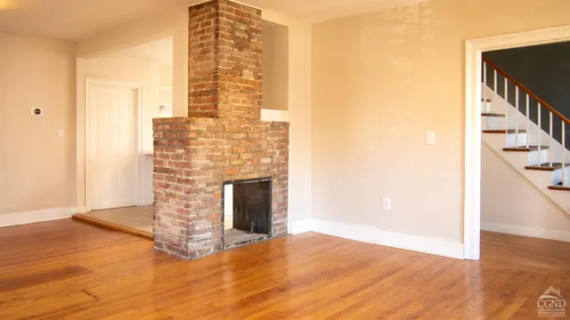 a view of an empty room with wooden floor and a fireplace