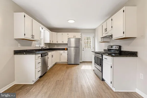 a kitchen with granite countertop a refrigerator oven a sink dishwasher and white cabinets with wooden floor