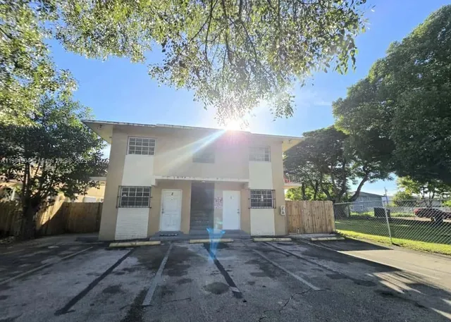 a view of a white house next to a yard with a large tree