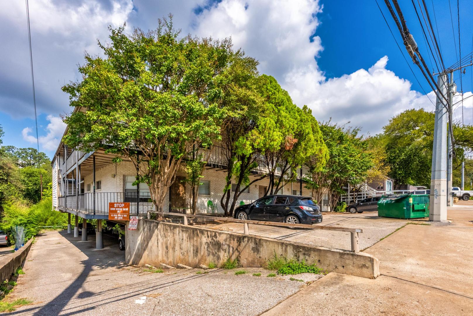 710 East Dean Keeton Street, Unit 207 Austin, TX 78705 - Photo 1 of 6 Multi-story building with a well-maintained exterior and private balconies, shaded by mature trees.