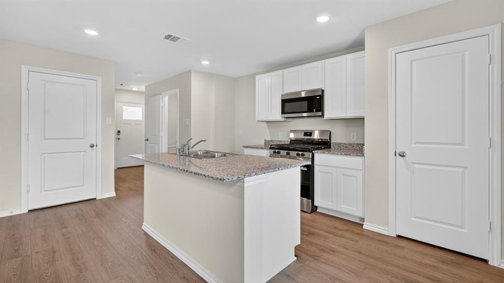 3534 Spring Time Street Forney, TX 75126 - Photo 3 of 24 Kitchen featuring an island with double basin sink, light granite countertops, white cabinetry, and stainless steel appliances including a gas range and microwave