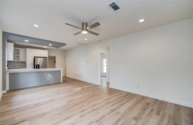 a view of an empty room with wooden floor and a ceiling fan