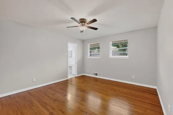 a view of an empty room with wooden floor and a ceiling fan