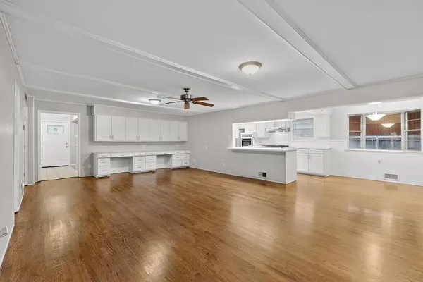 a view of an empty room with kitchen window and wooden floor