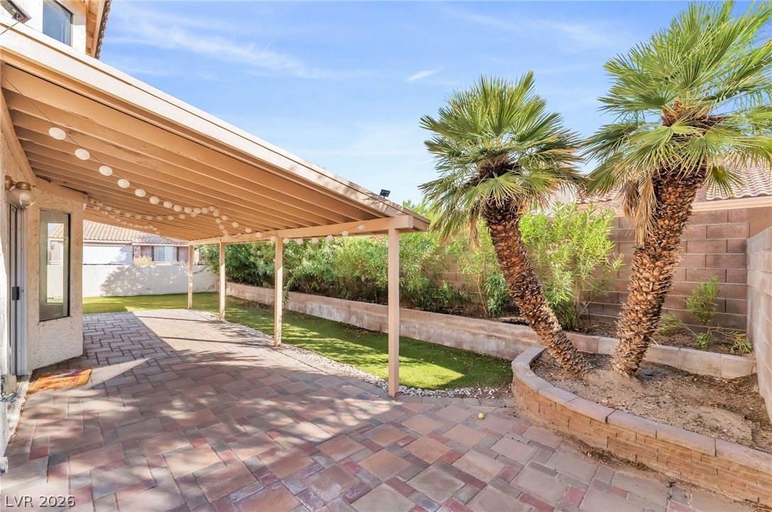 1402 Rim Fire Circle Henderson, NV 89014 - Photo 39 of 48 A spacious paved patio rests beneath a large covered structure alongside tropical palm trees.