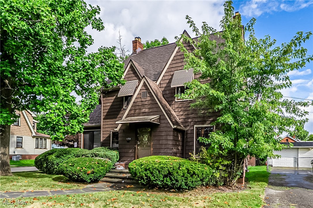 View of front facade featuring a chimney, a shingled roof, a front lawn, and an outbuilding