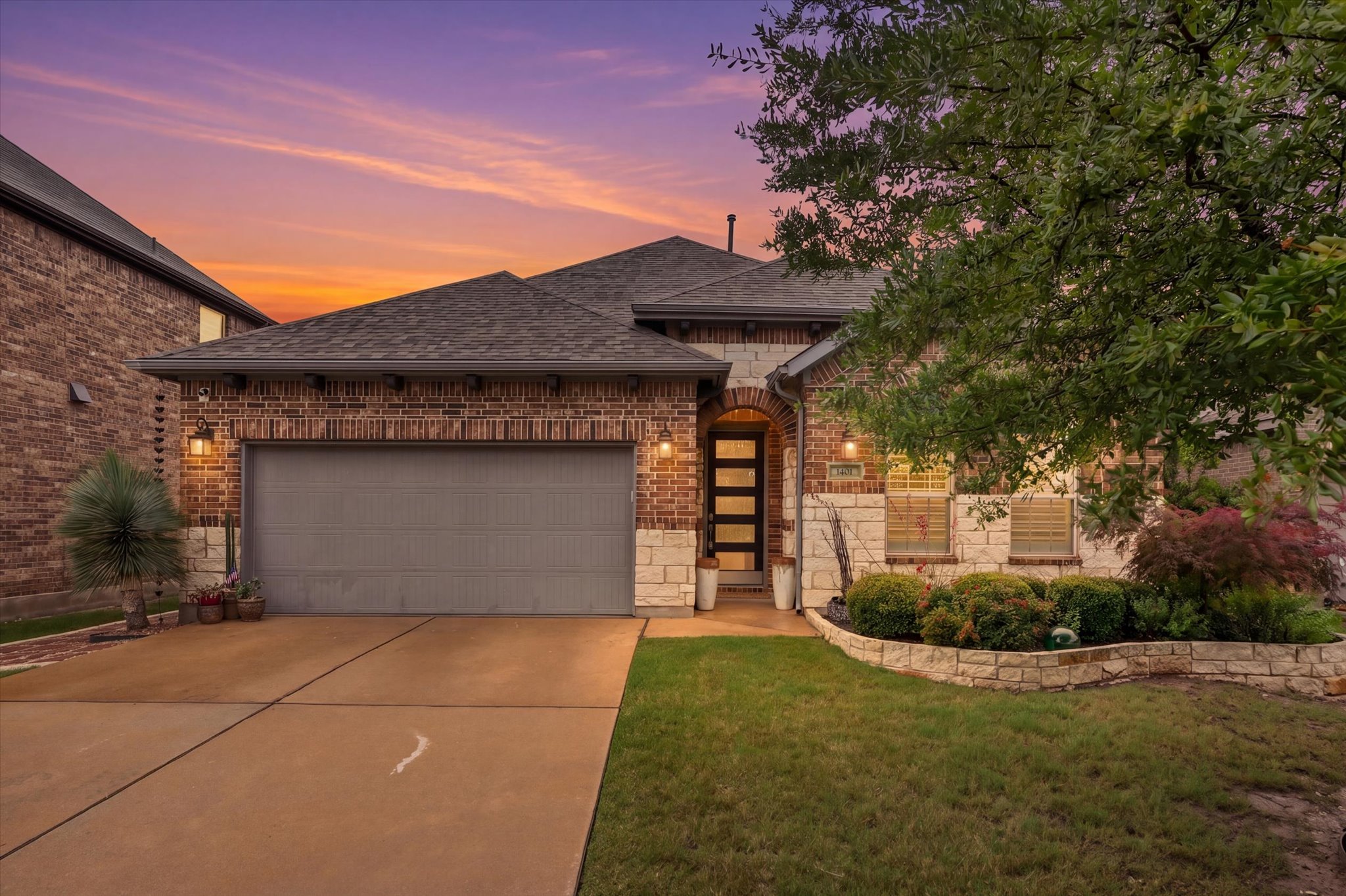 Brick and stone facade residence featuring a dark shingle roof and a two-car garage