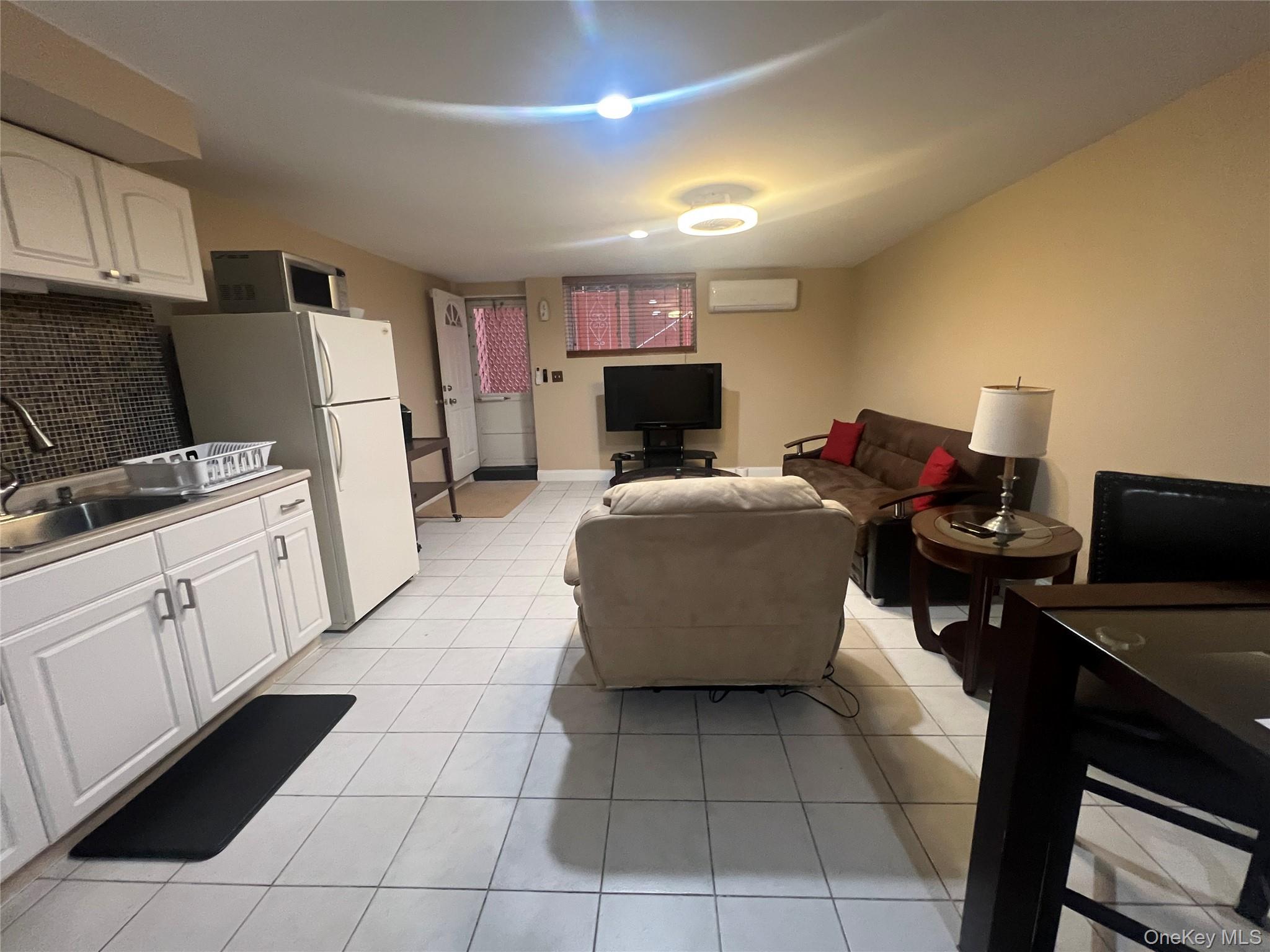 125-09 84th Road, Unit LL Queens, NY 11432 - Photo 2 of 7 a living room with furniture a flat screen tv and a refrigerator