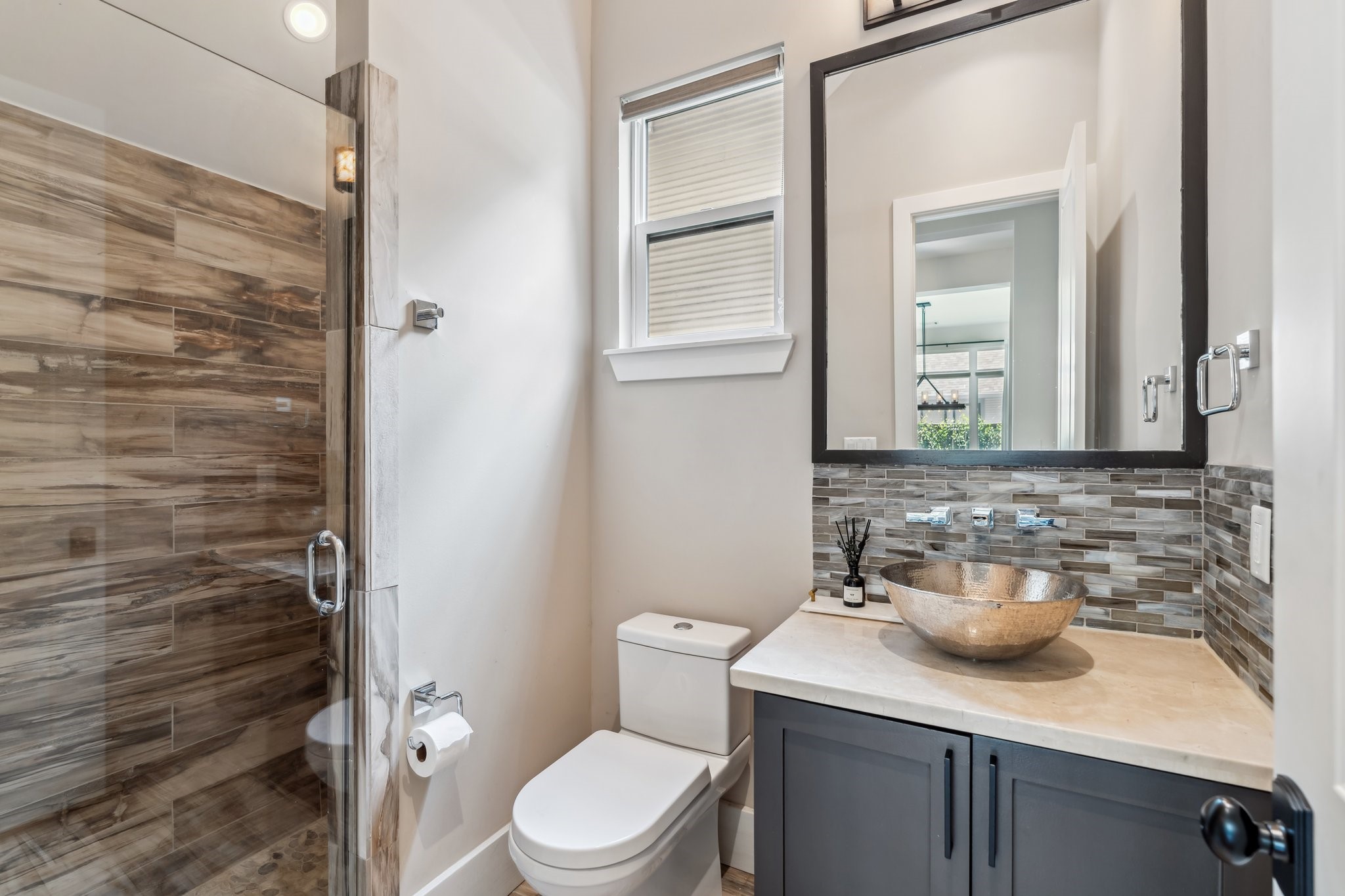 815 East 27th Street Houston, TX 77009 - Photo 15 of 44 This full bathroom, accessible from both the study/secondary bedroom and main living areas, features a sleek and functional design perfect for guests. The vanity offers convenient storage and is paired with a stylish vessel sink and wall-mounted faucet. A decorative mirror and vanity lights add an elegant touch, while the tile backsplash brings texture and contrast. The walk-in shower, complete with a bench seat, ensures comfort and convenience for guests.