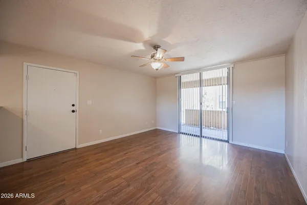 a view of an empty room with wooden floor and a ceiling fan