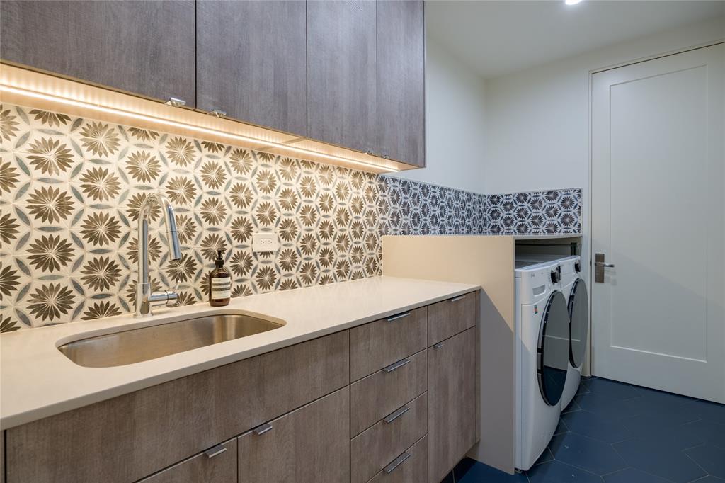 5736 Stonegate Road Dallas, TX 75209 - Photo 26 of 29 Laundry room featuring wood-finish cabinetry, under-cabinet lighting, a stainless steel sink with a gooseneck faucet, patterned tile backsplash, and hexagonal floor tiles