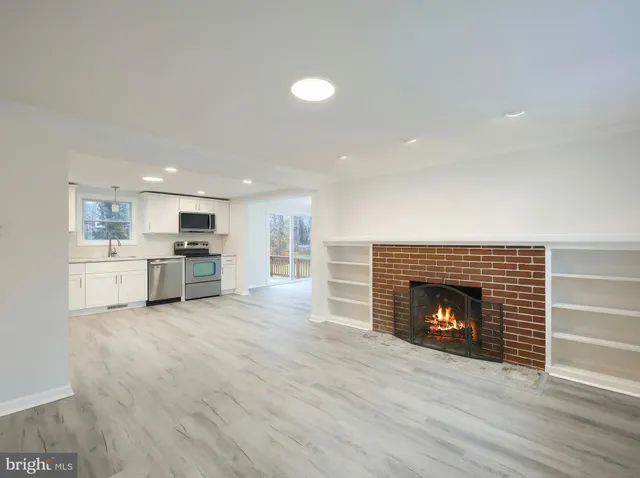 a view of an empty room with wooden floor fireplace and a window