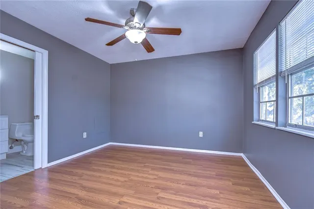 a view of an empty room with wooden floor and a ceiling fan