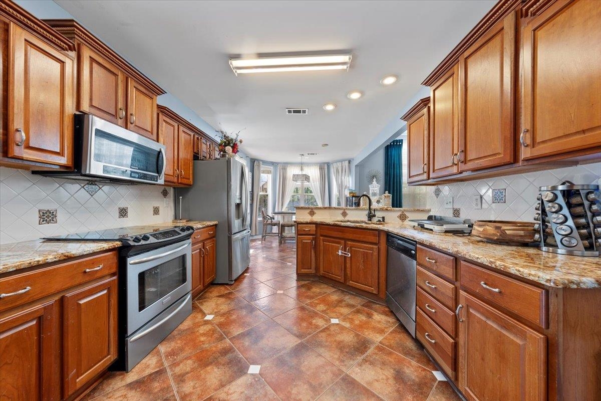 10941 Lubov Road Arlington, TN 38002 - Photo 11 of 39 a large kitchen with stainless steel appliances granite countertop a stove top oven a sink dishwasher a dining table and chairs with wooden cabinets