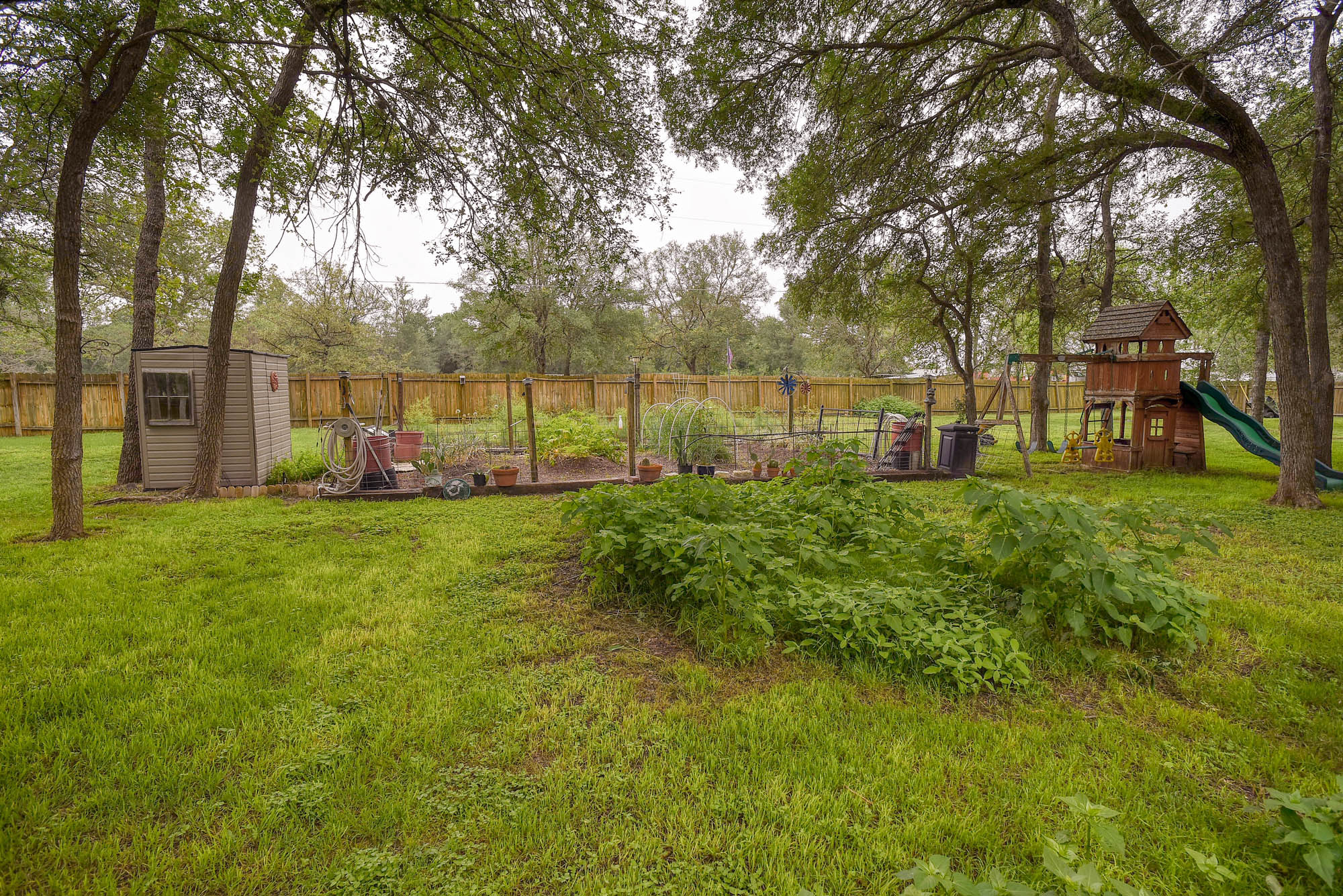 147 Spring Meadow Road Bastrop, TX 78602 - Photo 31 of 40 Spacious fenced backyard featuring a garden area, mature trees, and a storage shed