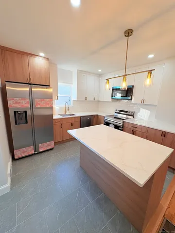 a large kitchen with kitchen island a stove a sink a refrigerator and white cabinets with wooden floor